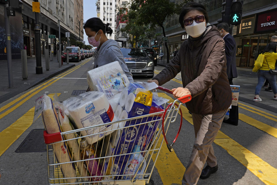 FILE - A woman pushes a grocery cart across a street after buying rice and and other supplies as residents worry about a shortage of food and supplies in Hong Kong on March 3, 2022. The fast-spreading omicron variant is overwhelming Hong Kong, prompting mass testing, quarantines, supermarket panic-buying and a shortage of hospital beds. Even the morgues are overflowing, forcing authorities to store bodies in refrigerated shipping containers. (AP Photo/Vincent Yu, File)