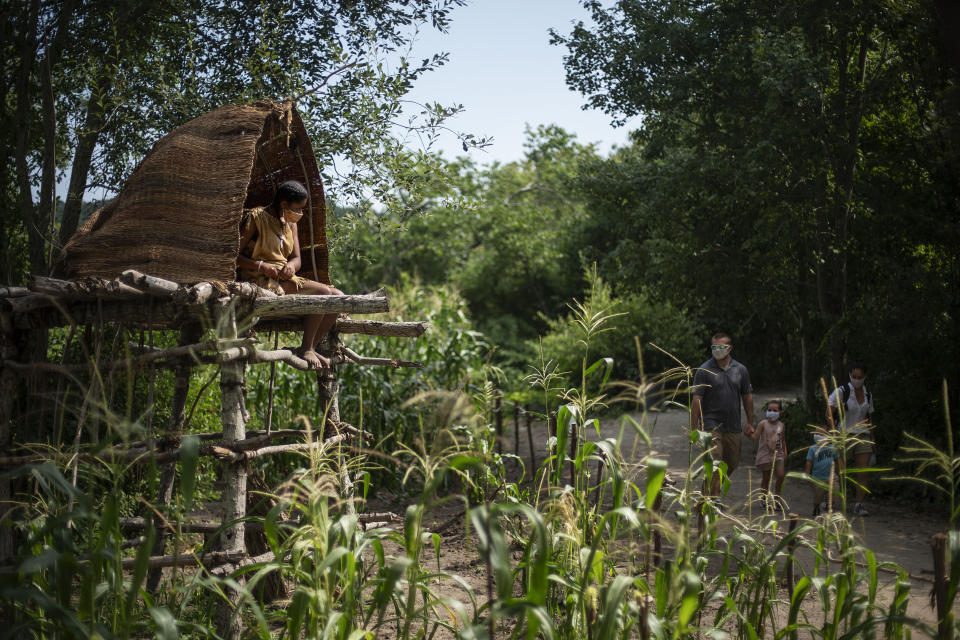 Alyssa Harris, a member of the Mashpee Wampanoags and a museum educator at Plimoth Plantation, a living history exhibit, sits in a corn watch tower as visitors walk through the Wampanoag Homesite, Wednesday, Aug. 12, 2020, in Plymouth, Mass. A disease outbreak that wiped out large numbers of the Native inhabitants of what is now New England gave the Pilgrims a beachhead in the "New World." So, some historians find it ironic that a pandemic has put many of the 400th anniversary commemorations of the Mayflower's landing on hold. (AP Photo/David Goldman)