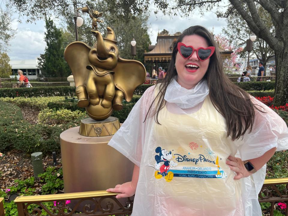megan posing with a gold dumbo statue in magic kingdom while wearing a disney poncho