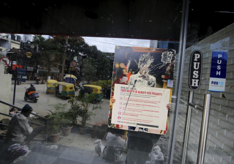 A distorted poster remains on the glass entrance of a famous pizza outlet which closed down recently due to pandemic in Bengaluru, India, Thursday, Oct. 15, 2020. Thousands of students and professionals who worked for IT companies and lived in the area have moved back to their native places to work remotely. Even as much of the Indian economy has reopened, Bengaluru’s professional workforce is returning to work at a much slower pace than those in most other major cities, raising the risk that the city faces a more protracted recovery. (AP Photo/Aijaz Rahi)