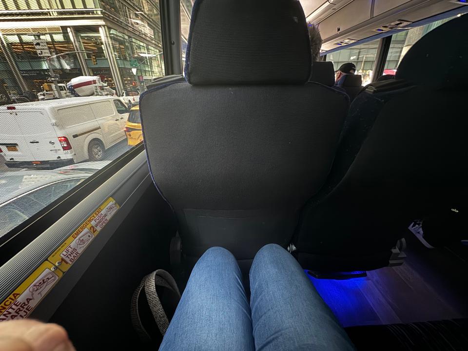 pair of legs sitting in a standard bus seat on the jitney in new york city