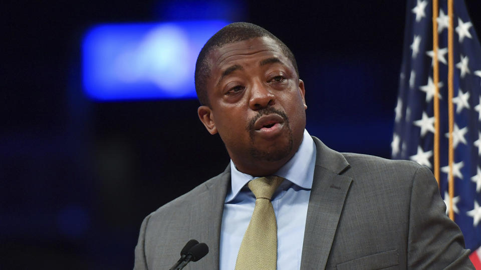 Brian Benjamin speaks behind a microphone and in front of a U.S. flag.