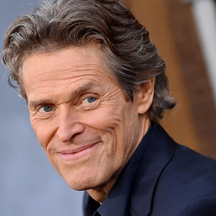 Willem Dafoe smiles on the red carpet