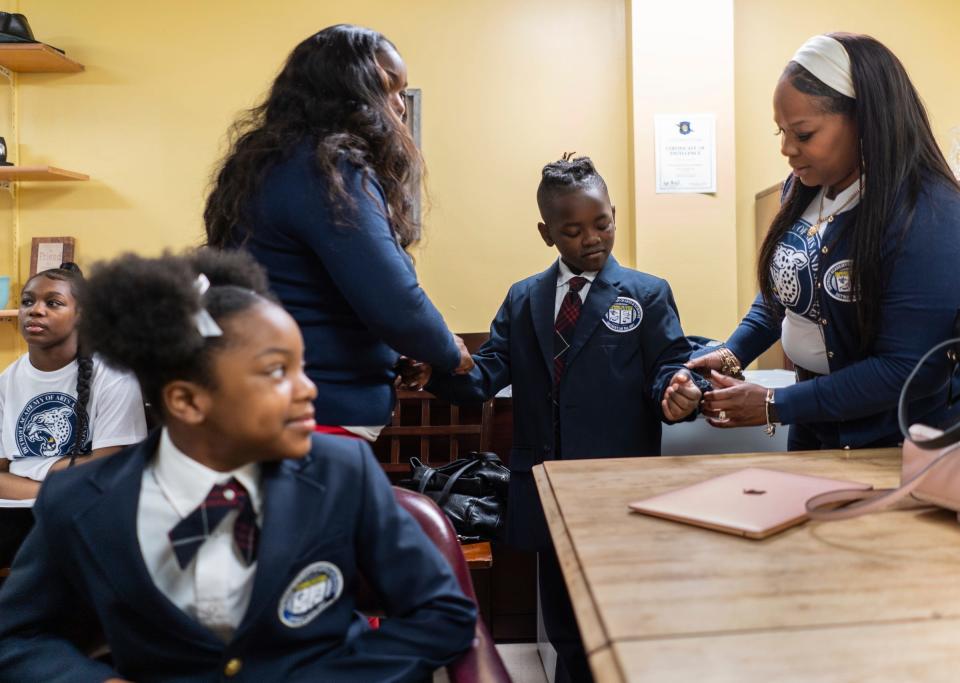 Detroit Academy of Arts and Sciences student Kyle Barginere gets help with his jacket from Toria Boyd, left, and Krystle Sims, right, before standing in during a press conference at the school on Detroit's east side on Thursday, May 25, 2023, announcing plans to hire qualifying teachers a $100,000 salary if they meet the criteria. 