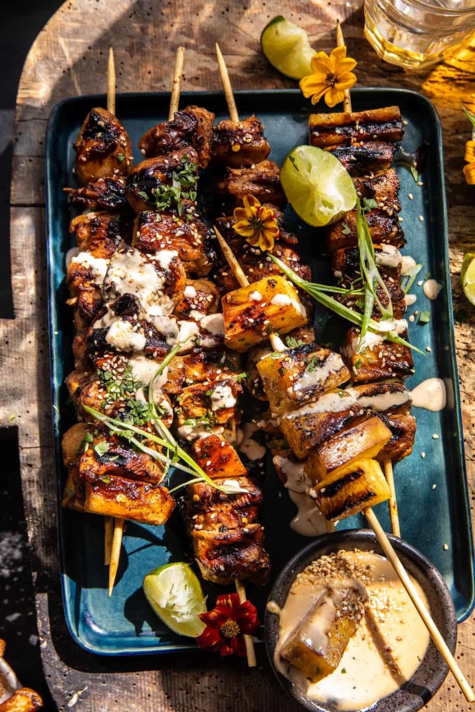 Grilled skewers with meat cubes and vegetables on a plate, garnished with herbs and sauces, accompanied by lime wedges and dipping sauce