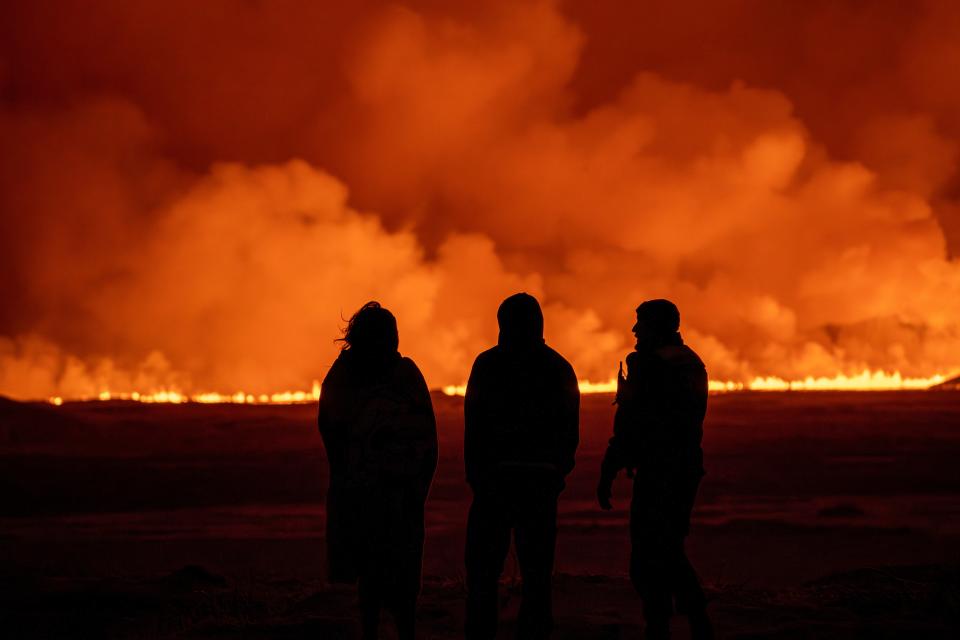 People watch as the night sky is illuminated caused by the eruption of a volcano in Grindavik on Iceland's Reykjanes Peninsula, Monday, Dec. 18, 2023 (Copyright 2023 The Associated Press. All rights reserved.)