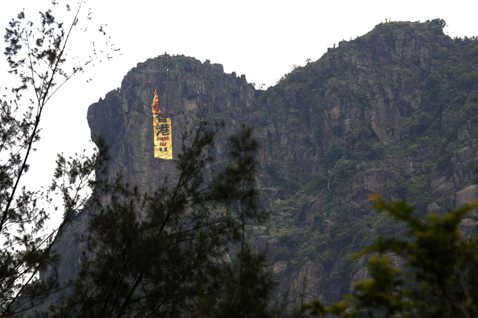 Firefighters remove a yellow banner with the words "Fight for Hong Kong" in Chinese and English which is hung on the Lion Rock mountain by pro-democracy protesters in Hong Kong, Sunday, June 16, 2019. Hong Kong was bracing Sunday for another massive protest over an unpopular extradition bill that has highlighted the territory's apprehension about relations with mainland China, a week after the crisis brought as many as 1 million into the streets. (AP Photo/Kin Cheung)