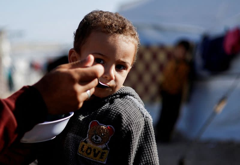 Un niño palestino desplazado, que huyó de sus casas debido a los ataques israelíes, recibe alimentos en un campamento de tiendas de campaña, en medio del conflicto en curso entre Israel y el grupo islamista palestino Hamás, en Ráfah, en el sur de la Franja de Gaza