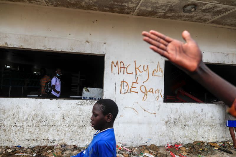 A boy walks past a graffiti that reads "Macky get out", in Dakar