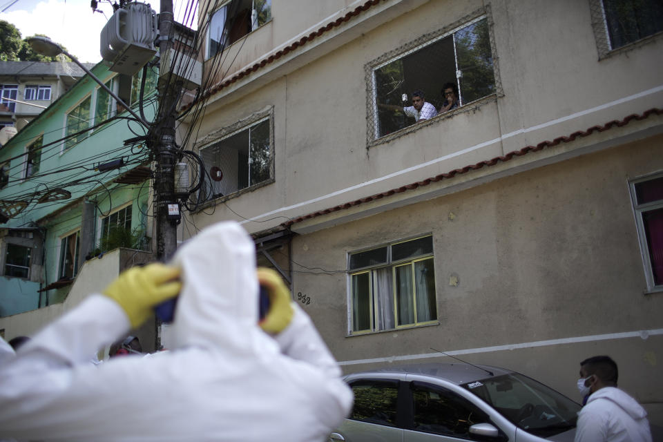 Residents watch water utility workers from CEDAE disinfecting the Vidigal favela in an effort to curb the spread of the new coronavirus, in Rio de Janeiro, Brazil, Friday, April 24, 2020. (AP Photo/Silvia Izquierdo)