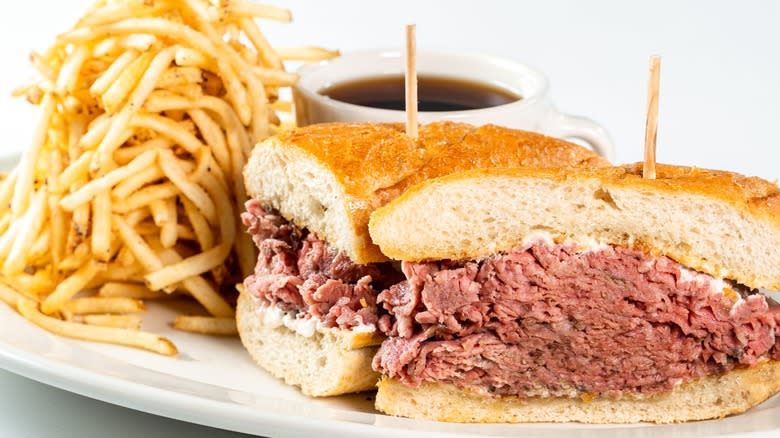 A French dip sandwich held together with toothpicks and plated with shoestring French fries and au jus
