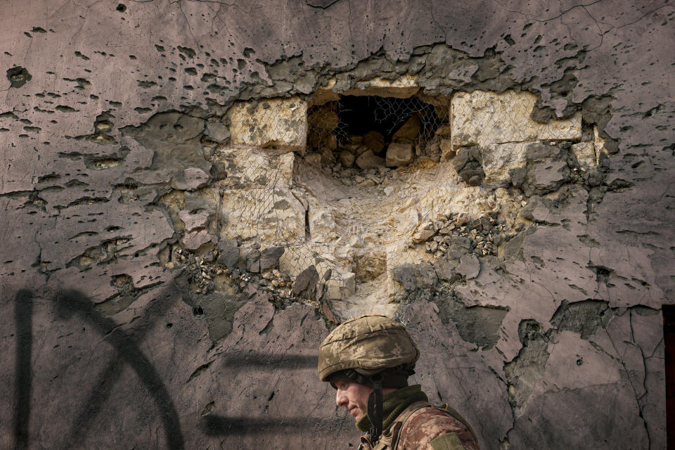 A Ukrainian serviceman walks by a building which was hit by a large caliber mortar shell in the frontline village of Krymske, Luhansk region, in eastern Ukraine, Saturday, Feb. 19, 2022. (AP Photo/Vadim Ghirda)