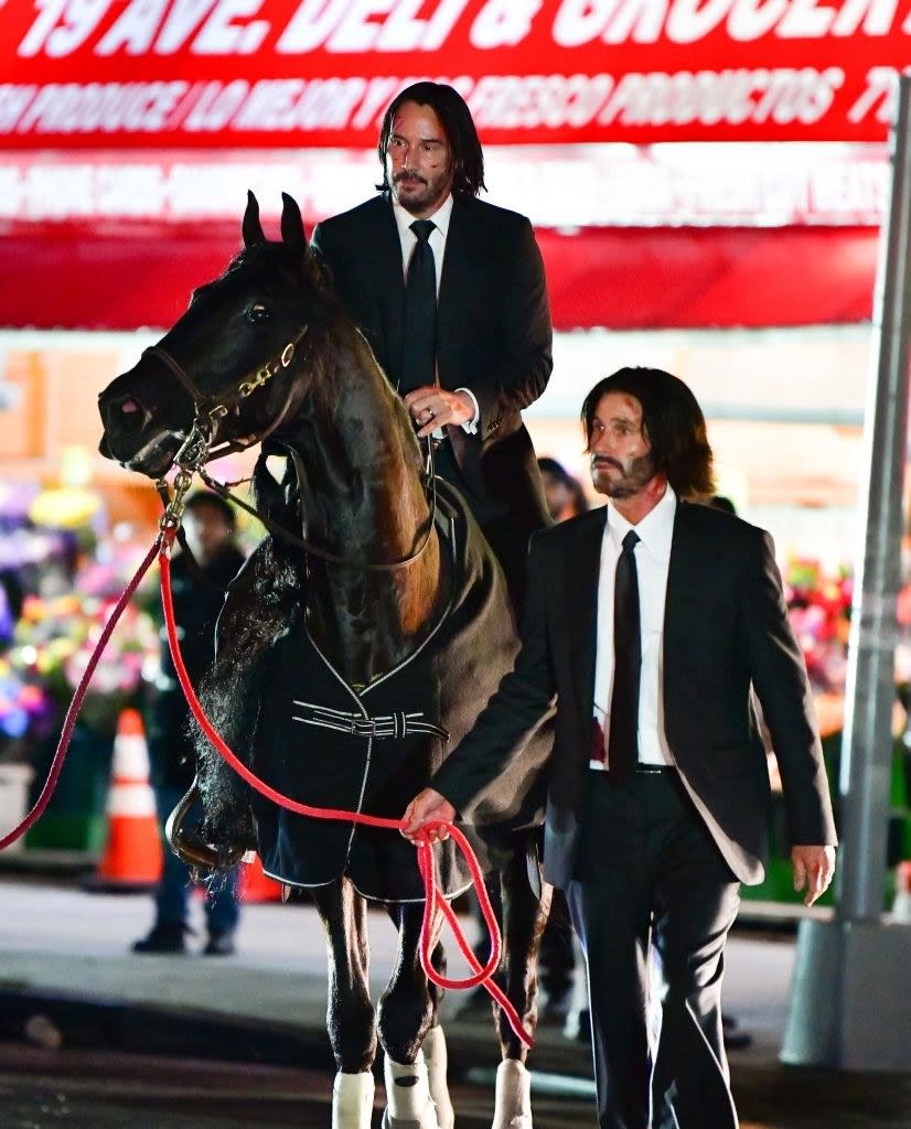Keanu on a horse with his body double walking beside them and holding the horse's rope