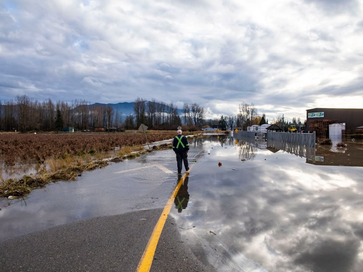 A contractor walks along a flooded road in the neighbourhood of Huntingdon in the Sumas Prairie flood zone in Abbotsford, B.C., on Monday. (Ben Nelms/CBC - image credit)