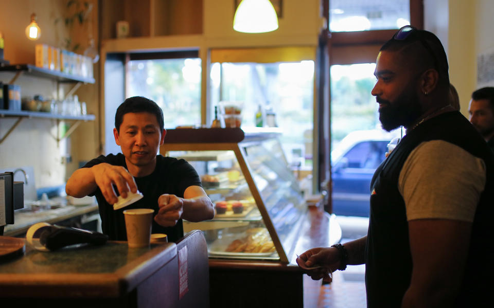 A cafe owner serves a takeaway coffee in Sydney to a customer.