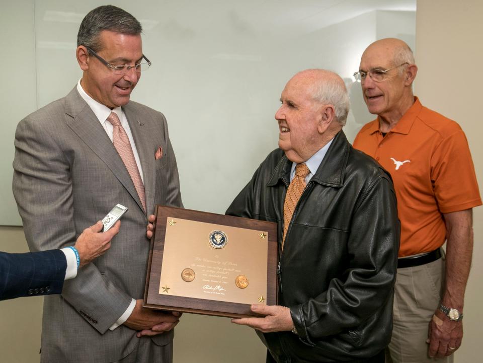 Former UT sports information director Bill Little presents a replica plaque to UT Athletic Director Chris Del Conte while Ted Koy, co-captain of the 1969 Longhorn football team, watches at Del Conte’s office in October of 2019. Little passed away Friday at age 81. He worked in the Texas athletic department for over 50 years.