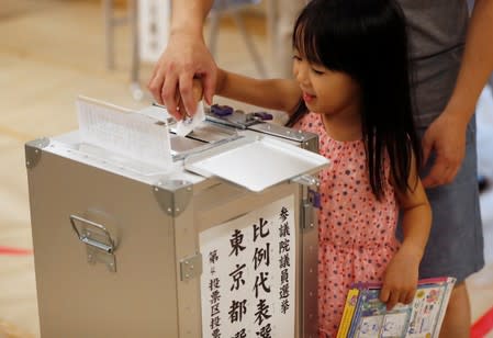 A girl helps to cast a ballot at a voting station during Japan's upper house election in Tokyo