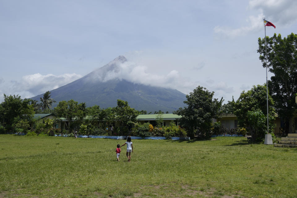 Mayon volcano is seen behind an evacuation center in Santo Domingo town, Albay province, northeastern Philippines, Tuesday, June 13, 2023. Truckloads of villagers on Tuesday fled from Philippine communities close to gently erupting Mayon volcano, traumatized by the sight of red-hot lava flowing down its crater and sporadic blasts of ash. (AP Photo/Aaron Favila)