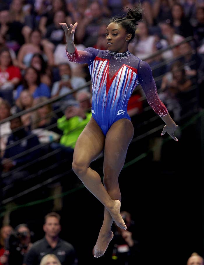 Simone Biles performs a gymnastics routine in a leotard with a sparkle design in front of an audience
