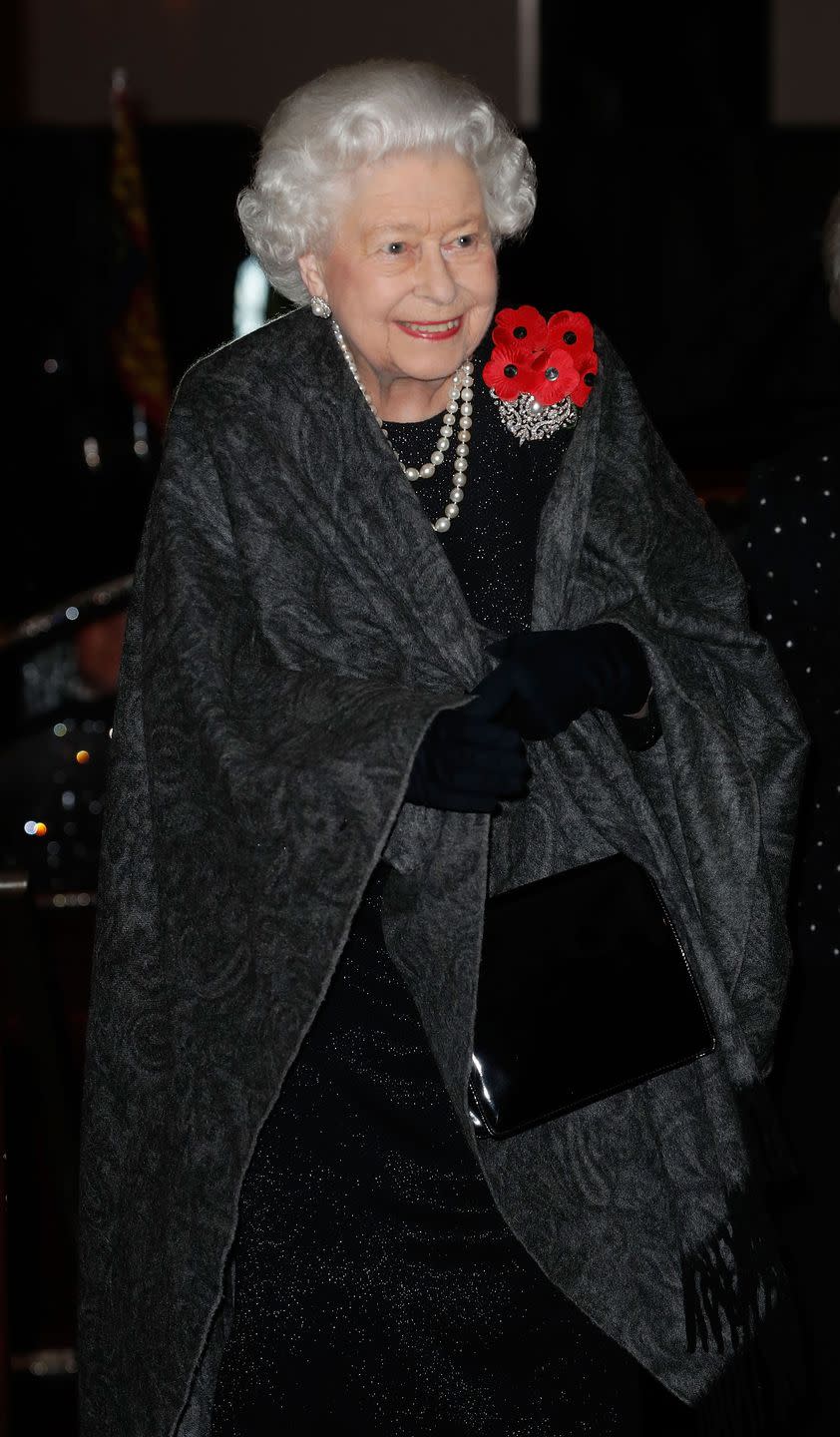 <p>The Queen makes her entrance, wearing a black dress and gray shawl, with pearls, a black handbag, and of course, a cluster of poppies.</p>