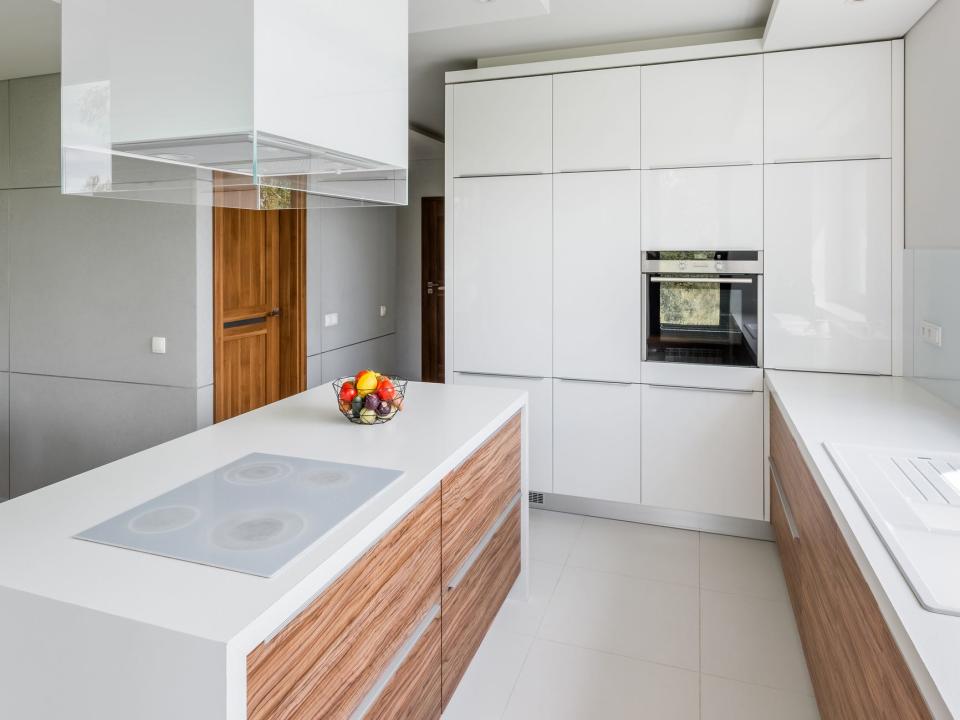 A mostly white kitchen with some wooden detailing on the counters. A large rectangular white light fixture hangs over a kitchen island