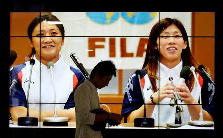 A man holding a wallet walks past an electronic board displaying a news photo of Japan's three-time Olympics wrestling gold medallists Saori Yoshida (R) and Kaori Icho as wrestling wins back its Olympic spot for the 2020 Tokyo Games at Tokyo train station September 9, 2013. J REUTERS/Yuya Shino