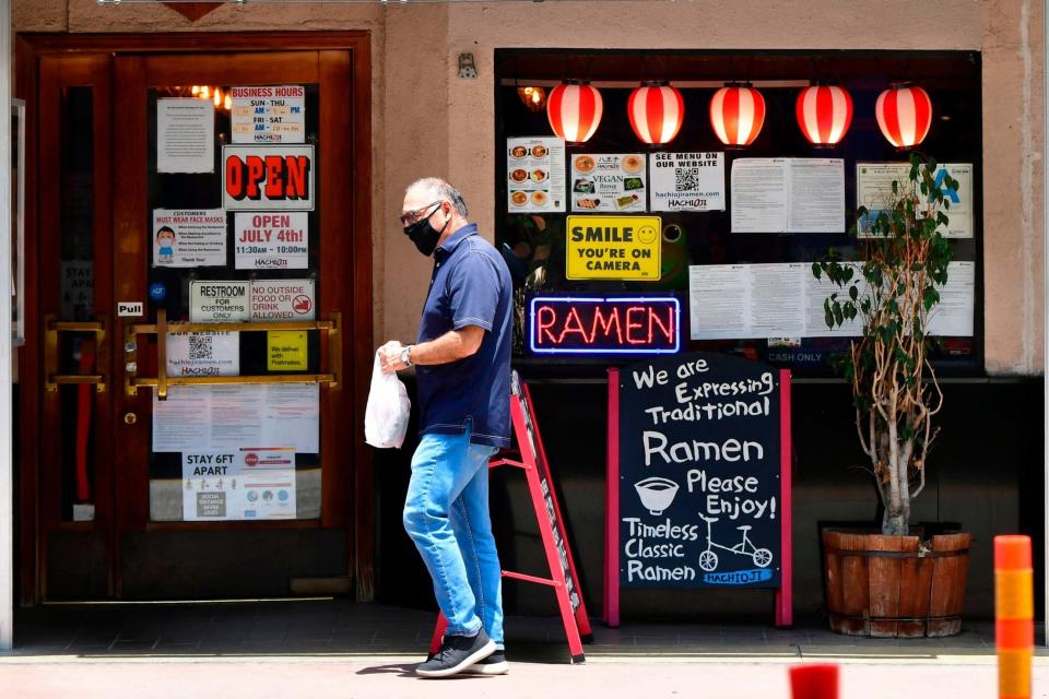 A man wearing a facemask walks past a Ramen restaurant in Los Angeles (AFP via Getty Images)