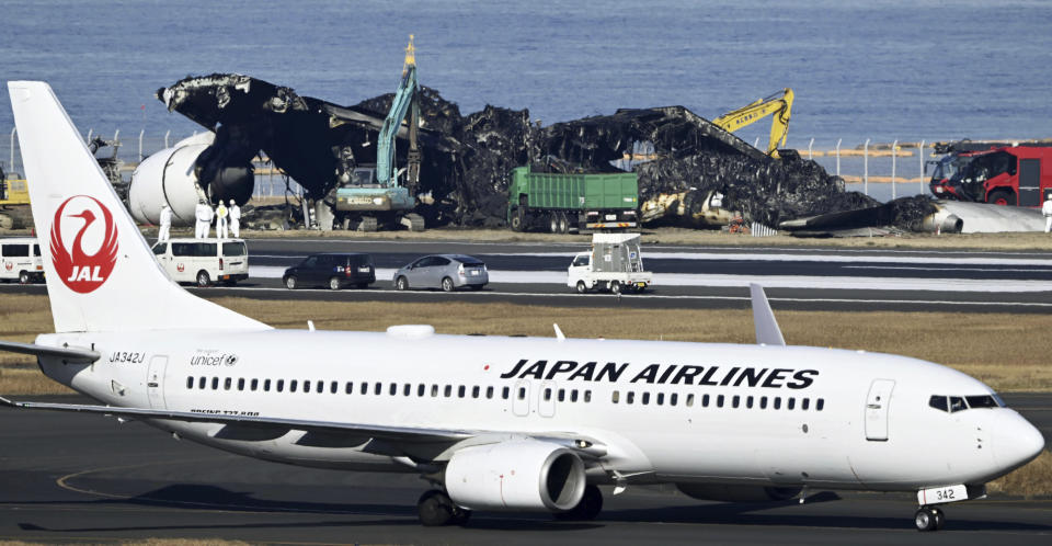 A Japan Airline plane moves past a removal work, rear, which is underway at the site of a planes collision at Haneda airport in Tokyo Friday, Jan. 5, 2024. Cranes were dismantling the Japan Airlines Flight 516 Airbus A350 that caught fire after hitting a Coast Guard aircraft while it was landing Tuesday at the airport. (Kyodo News via AP)