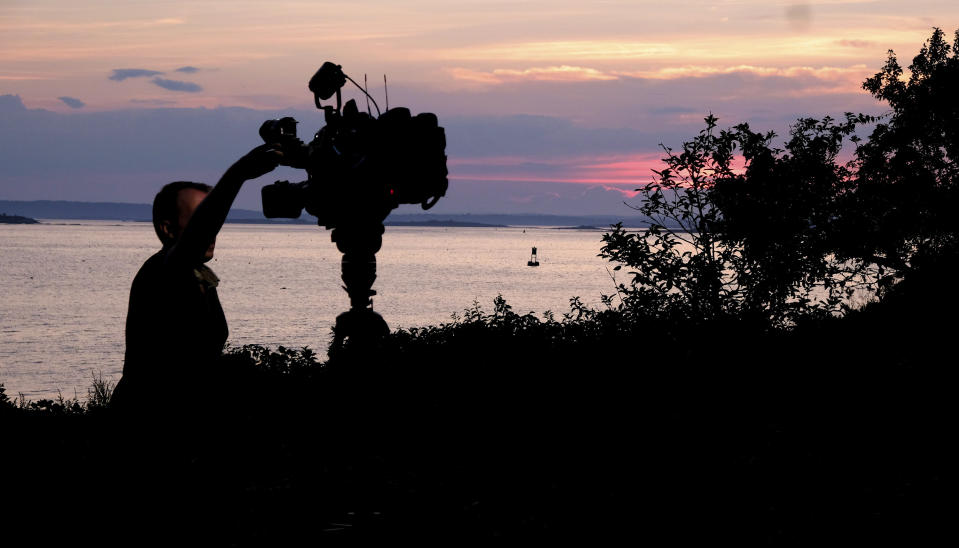 A member of a TV crew adjusts their camera while filming near the shore of Bailey Island, Maine, where a woman swimming off the coast was killed in an apparent shark attack Monday, July 27, 2020. Two kayakers helped the person get to shore, and an ambulance provided further assistance, but she was pronounced dead at the scene, Marine Patrol said. (AP Photo/Jim Gerberich)