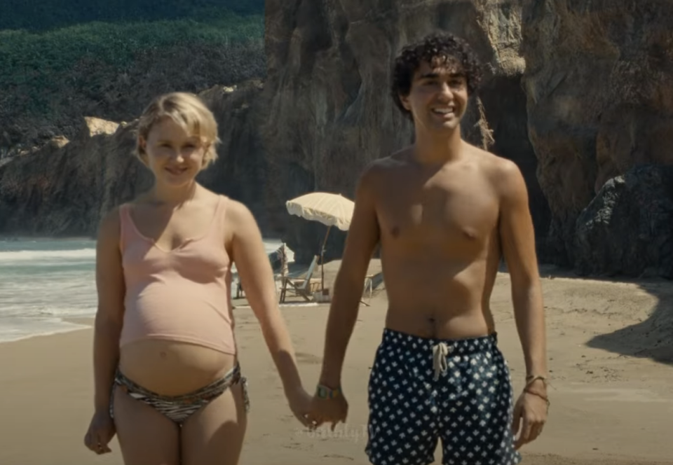 a pregnant woman holding hands with a guy on a beach