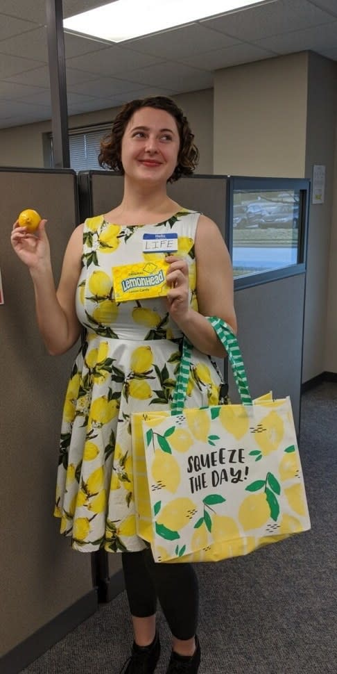 A woman in a lemon dress and a name tag reading "hello, my name is life" who is handing out lemons and lemonhead candy