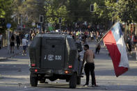 An anti-government protester with a Chilean flag looks into a police vehicle amid ongoing demonstrations triggered by an increase in subway fares in Santiago, Chile, Monday, Oct. 21, 2019. Protesters defied an emergency decree and confronted police in Chile's capital on Monday, continuing disturbances that have left at least 11 dead. (AP Photo/Miguel Arenas)