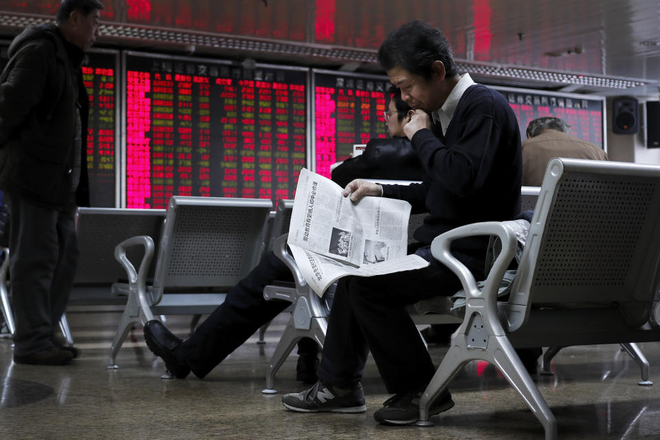 An investor reads a newspaper as others monitor stock prices at a brokerage house in Beijing, Friday, Dec. 6, 2019. Shares swung higher in Asia on Friday after a wobbly day of trading on Wall Street as investors awaited a U.S. government jobs report and kept an eye out for developments in China-U.S. trade talks. (AP Photo/Andy Wong)