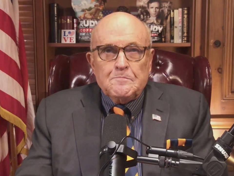 Giuliani sitting in front of his shelf featuring self-branded coffee (‘America’s Mayor Live' / screengrab)