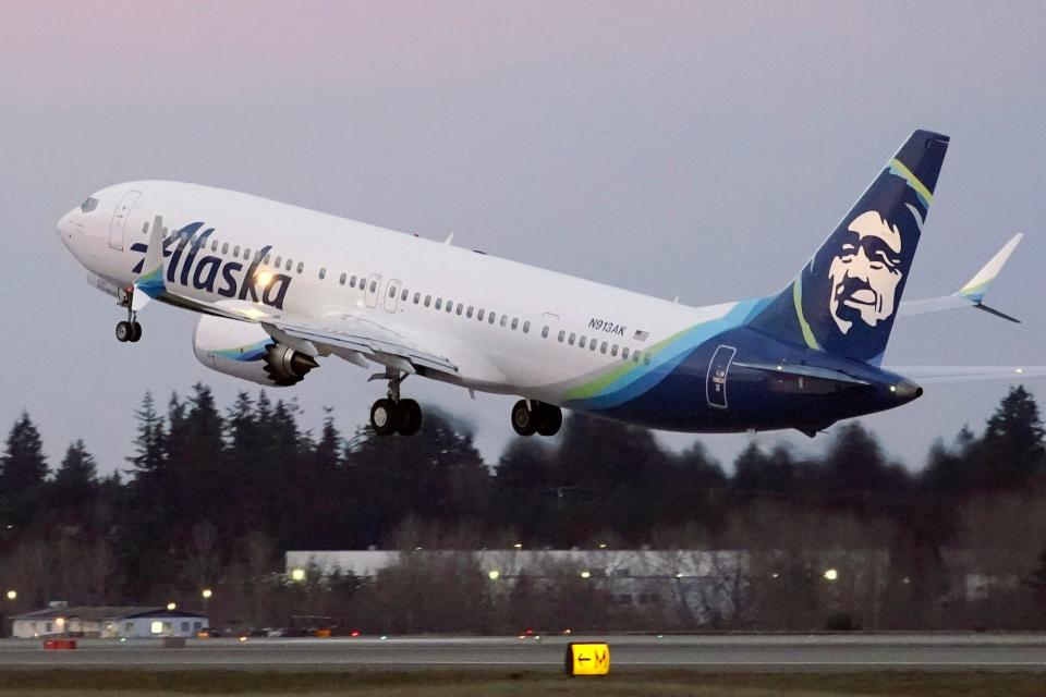 A white Alaska Airlines plane with blue details takes off.