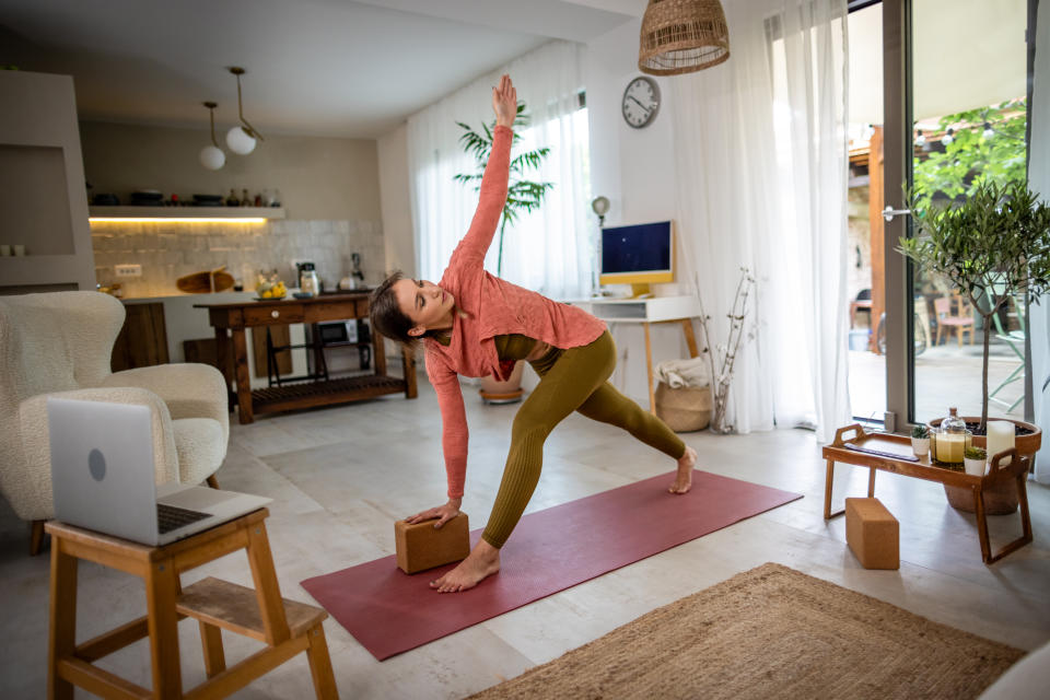 Photo of young woman doing online yoga in a living room at home.