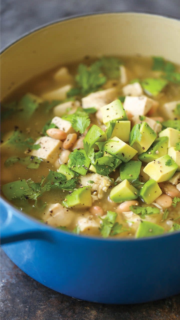 A Dutch oven filled with chunky chicken and white bean stew with avocado and cilantro