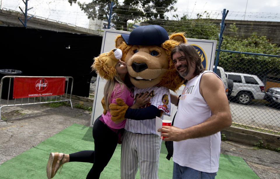 In this Oct. 12, 2018 photo, baseball fans of Leones de Caracas pose with the team's mascot prior the season's opening game against the Tiburones de la Guaira in Caracas, Venezuela. Last year's stadium attendance rose 5 percent amid the political and economic crisis, although it remains down by a third from a peak in the 2013-2014 season. (AP Photo/Fernando Llano)