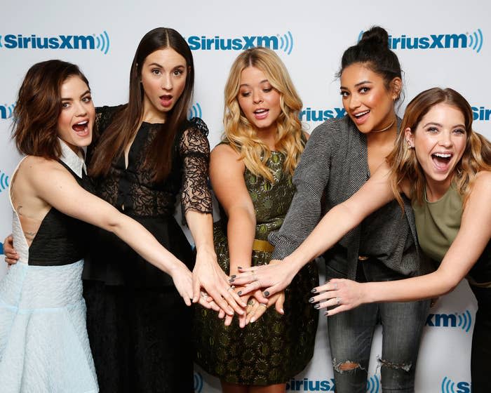 Lucy Hale, Troian Bellisario, Sasha Pieterse, Shay Mitchell, and Ashley Benson pose together with their hands in the center at a SiriusXM event