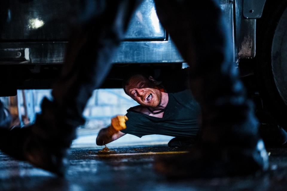 A man yells while lying underneath a vehicle