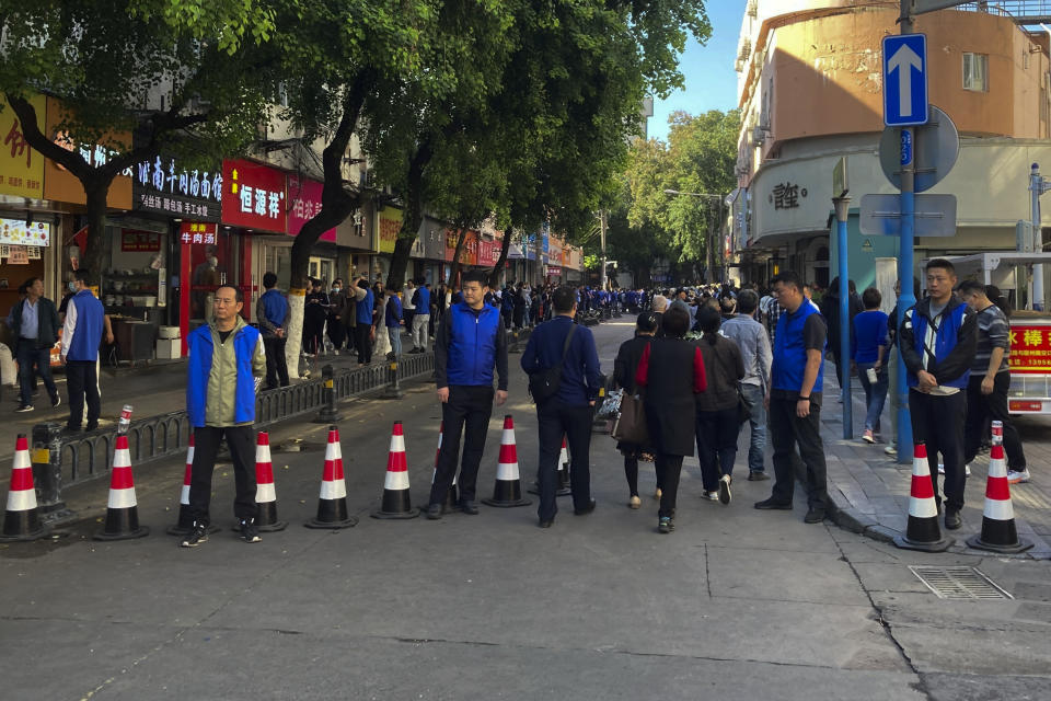 Security personnel in blue vest stand watch as residents with flowers head to a residential building where the late Chinese Premier Li Keqiang spent his childhood in Hefei city, in central China's Anhui province, Thursday, Nov. 2, 2023. Hundreds, possibly thousands, of people gathered near a state funeral home Thursday as former Premier Li Keqiang was being put to rest. (AP Photo/Ken Moritsugu)