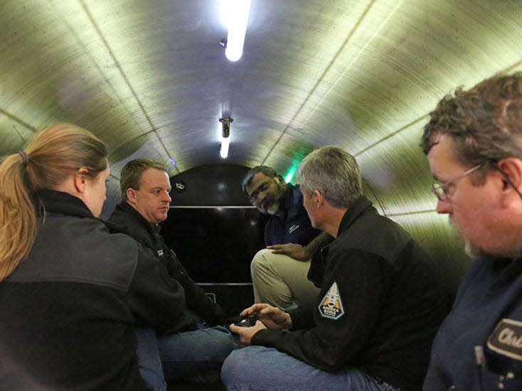 Five crew members, comprising four men and one woman, sitting cross-legged inside the Titan submersible.