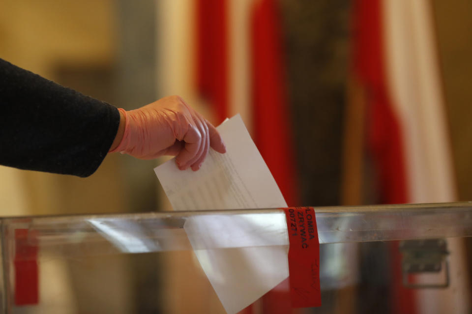 A resident, wearing protective gloves, casts a vote during presidential election in Warsaw, Poland, Sunday, June 28, 2020. The election will test the popularity of incumbent President Andrzej Duda who is seeking a second term and of the conservative ruling party that backs him. (AP Photo/Petr David Josek)