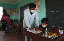 Teacher Manuel Layme works with a student, both wearing new protective uniforms, during the first week back to in-person classes amid the COVID-19 pandemic, as a parent, left, observes class in the Aymara Indigenous community near Jesus de Machaca, Bolivia, Thursday, Feb. 4, 2021. (AP Photo/Juan Karita)