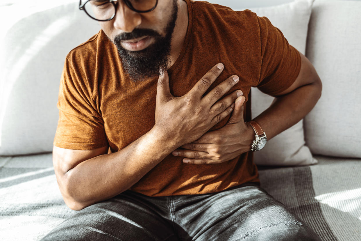 A man sitting on a couch clutches his chest in pain.