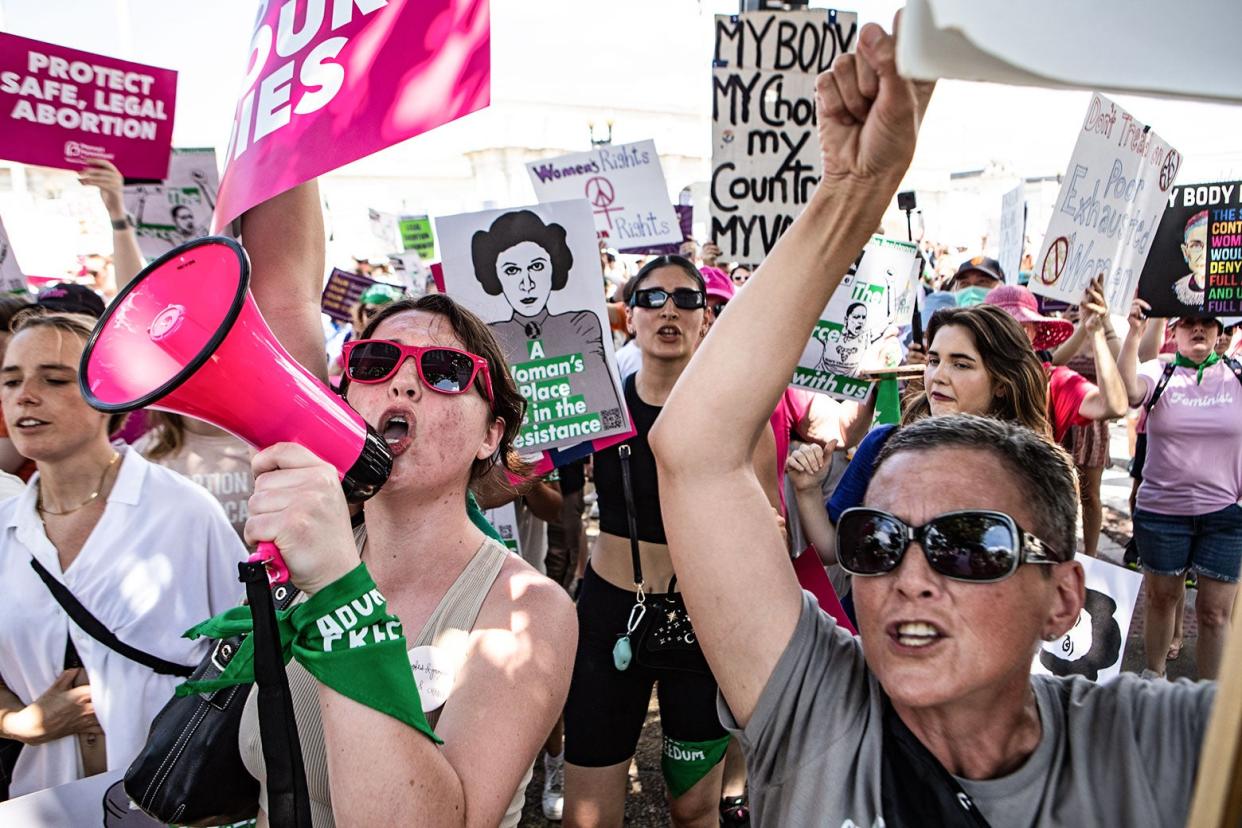 Women hold bullhorns and signs reading, for example, "Protect safe, legal abortion."