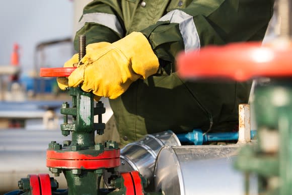 A worker in a coat and yellow work gloves turning a valve.