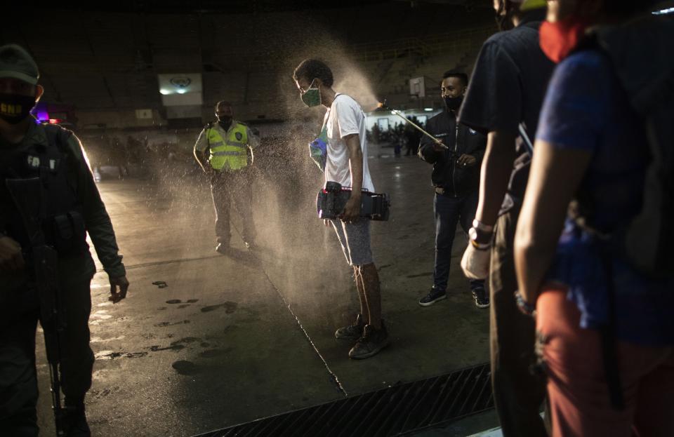 A man who was detained for not complying with COVID-19 regulations by breaking curfew and being out on the street drinking, is disinfected with an alcohol solution after he was transported to a coliseum in the Petare neighborhood of Caracas, Venezuela, early Saturday, Aug. 8, 2020, as part of an operation to educate residents on the risks of being out and socializing in groups amid the new coronavirus pandemic. Residents are released a few hours later after receiving instruction on best social distancing practices. (AP Photo/Ariana Cubillos)