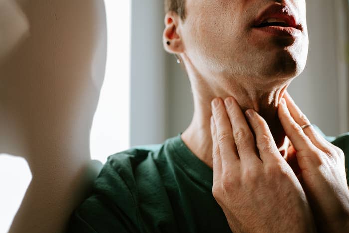 Man in green shirt touching his throat, looks uncomfortable, possibly indicating sore throat or discomfort