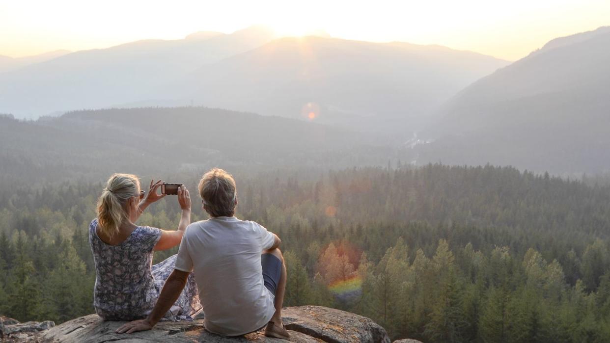 mature couple relax on mountain ledge, look out to view